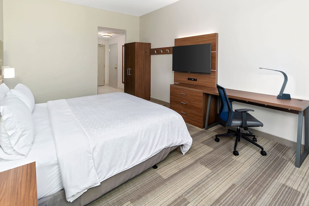 A hotel room with a bed, a desk with a computer, a chair, a TV, and a wardrobe.