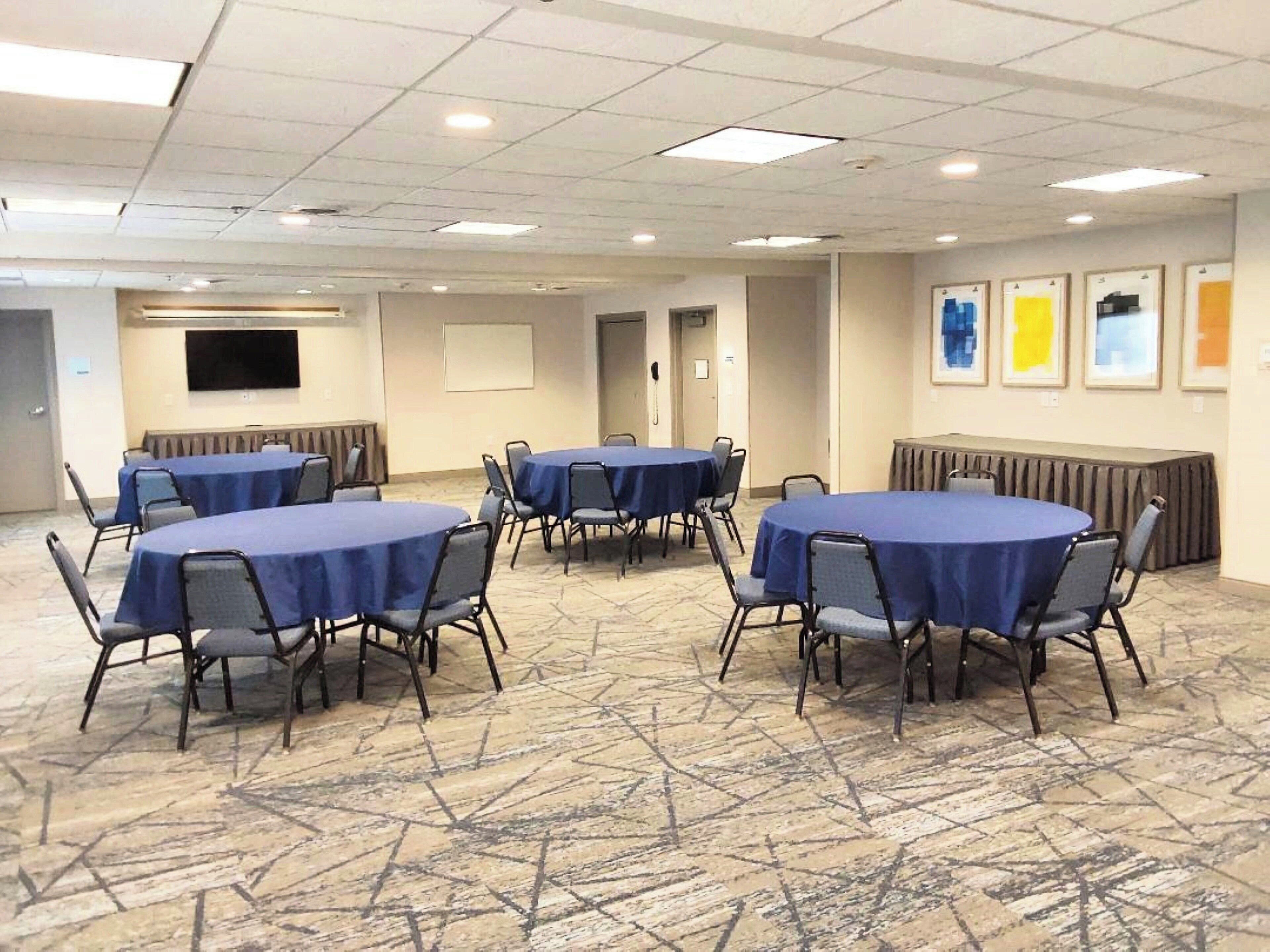 A conference room with multiple round tables and chairs, a flat-screen TV, and framed artwork on the walls.