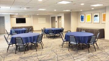 A conference room with multiple round tables and chairs, a flat-screen TV, and framed artwork on the walls.