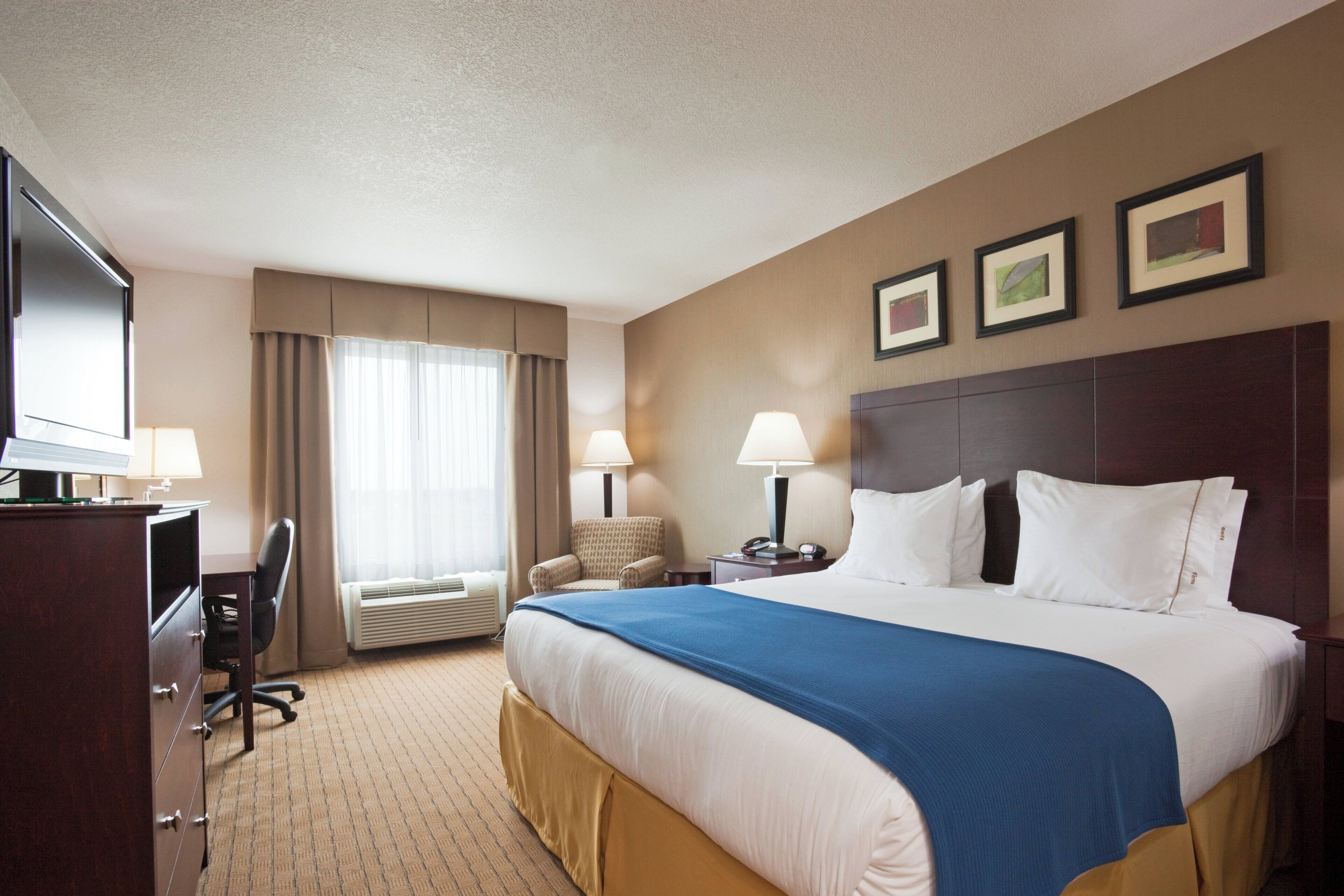 A hotel room with a bed, desk, chair, and a TV.