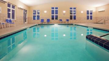 A swimming pool with clear blue water, surrounded by lounge chairs and a tiled wall.