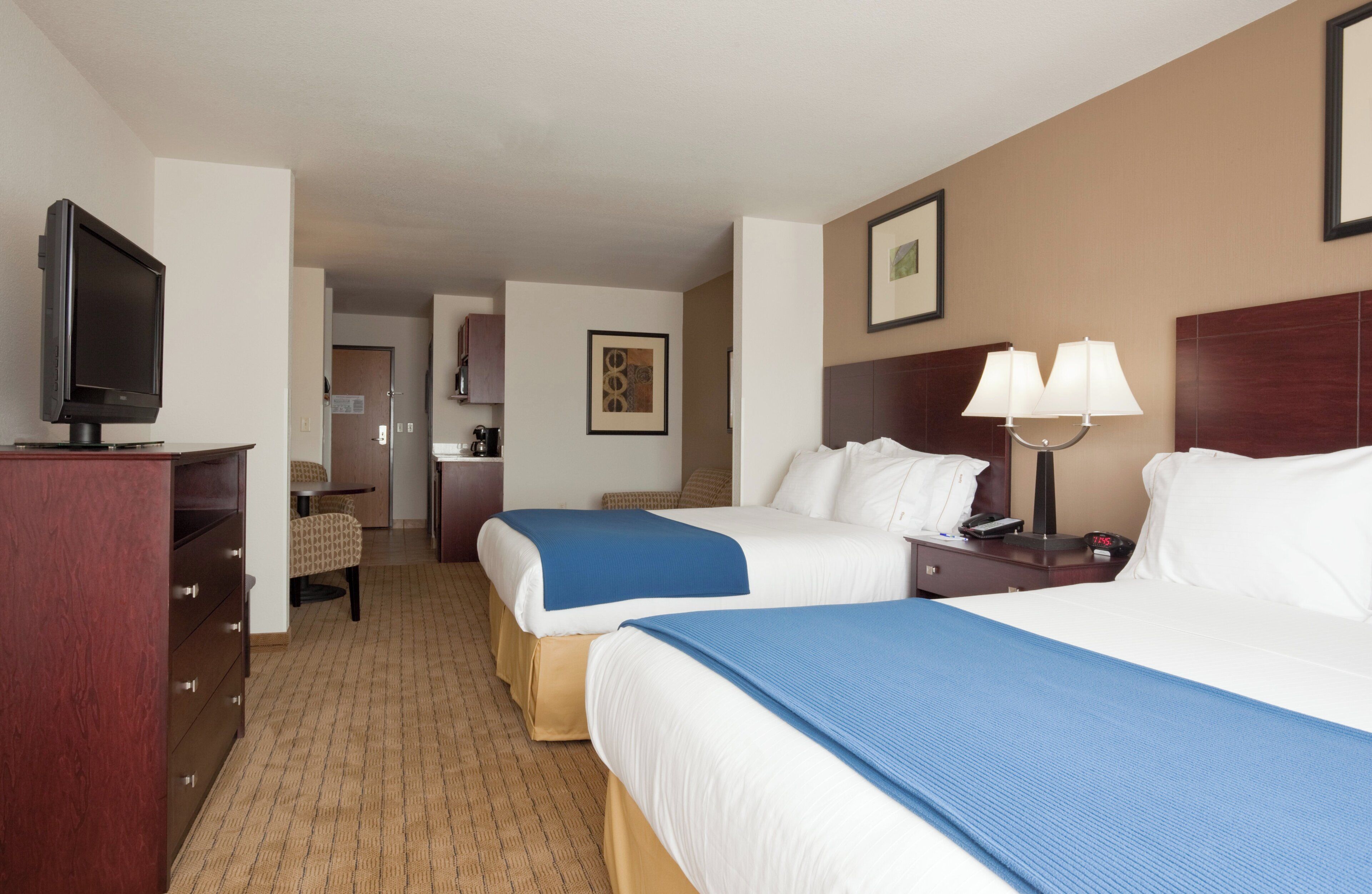 Une chambre d’hôtel avec deux lits, un bureau, une télévision et une salle de bain visible à travers une porte ouverte.