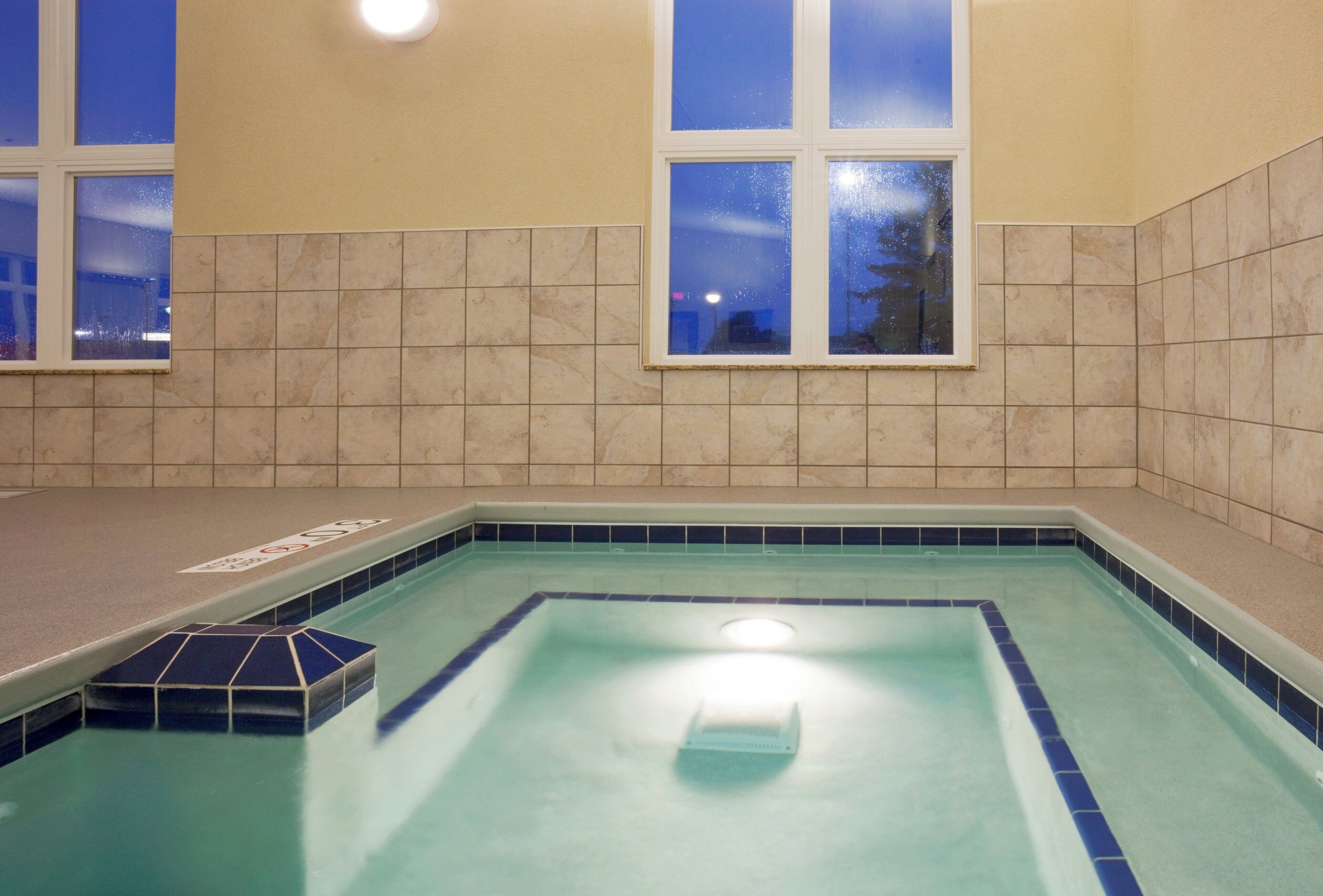 Una piscina interior con agua azul cristalina, rodeada de azulejos color beige y un borde alicatado.