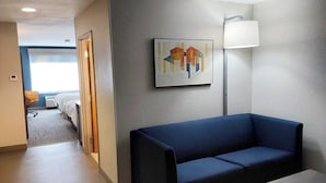 Hotellihuoneessa on sininen sohva, pieni pöytä, lamppu ja seinällä taulu.