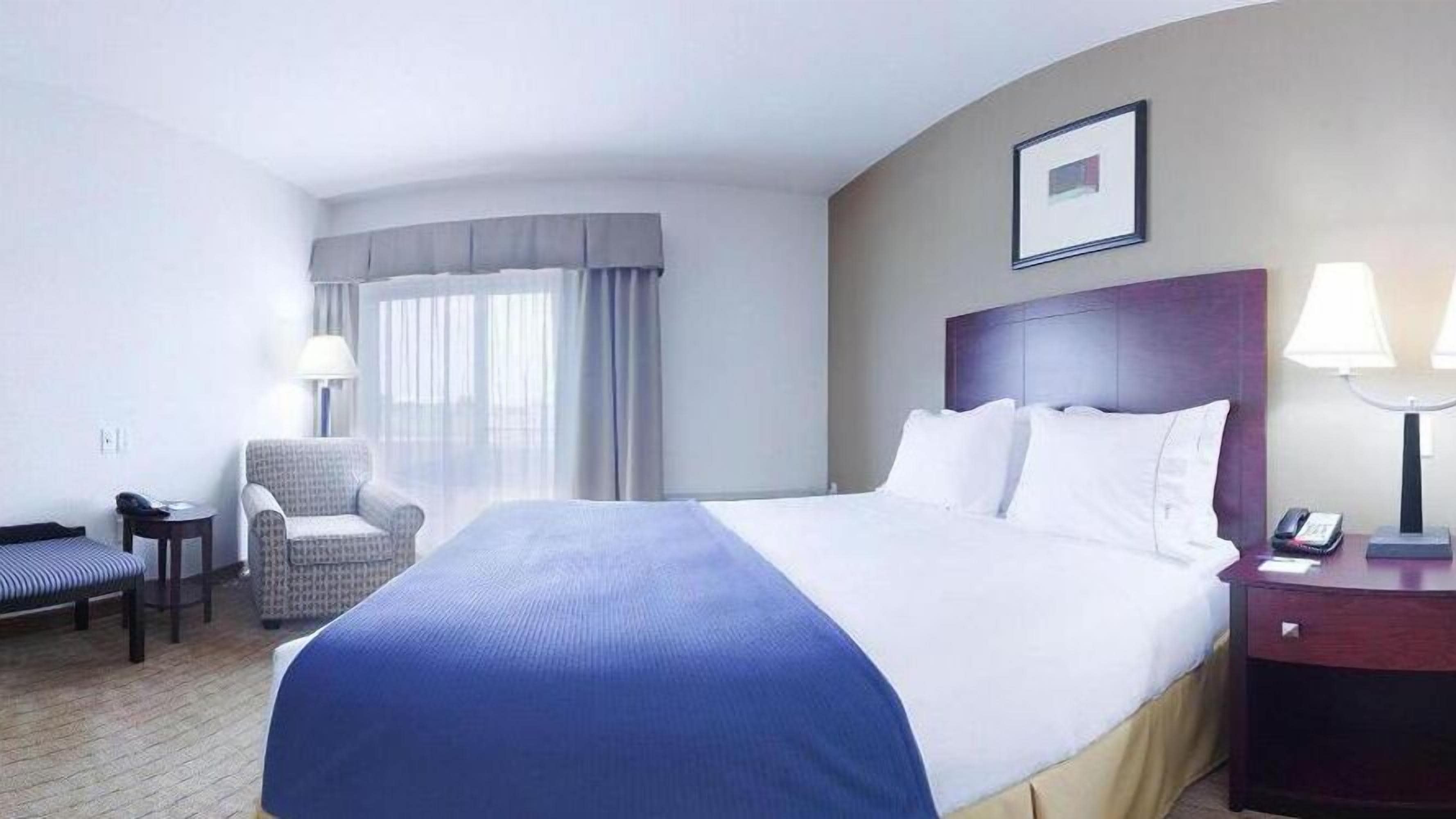 Una habitación de hotel con una cama grande, una silla, un escritorio y una mesita de noche.