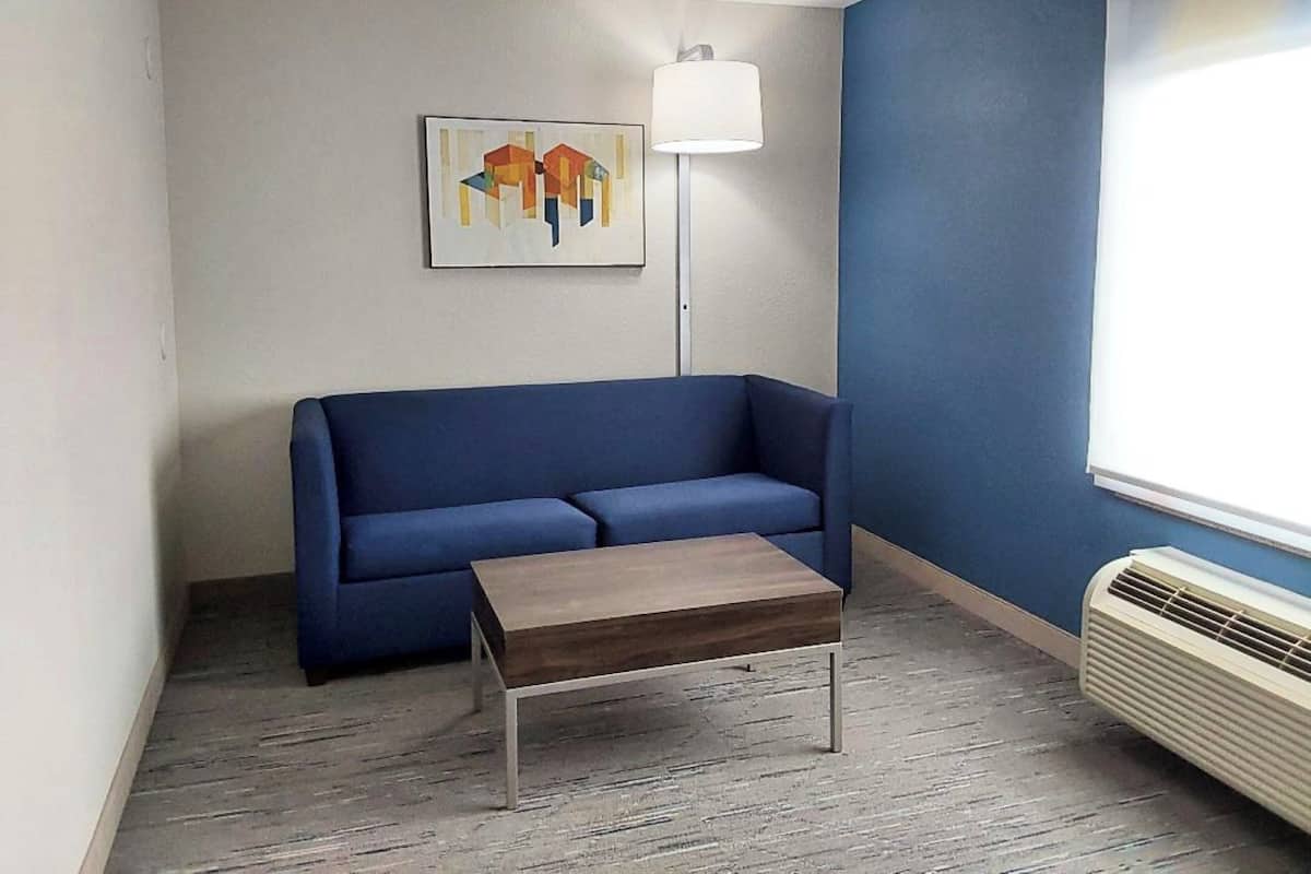 A room with a blue sofa, a wooden coffee table, a floor lamp, and a window with an air conditioner.
