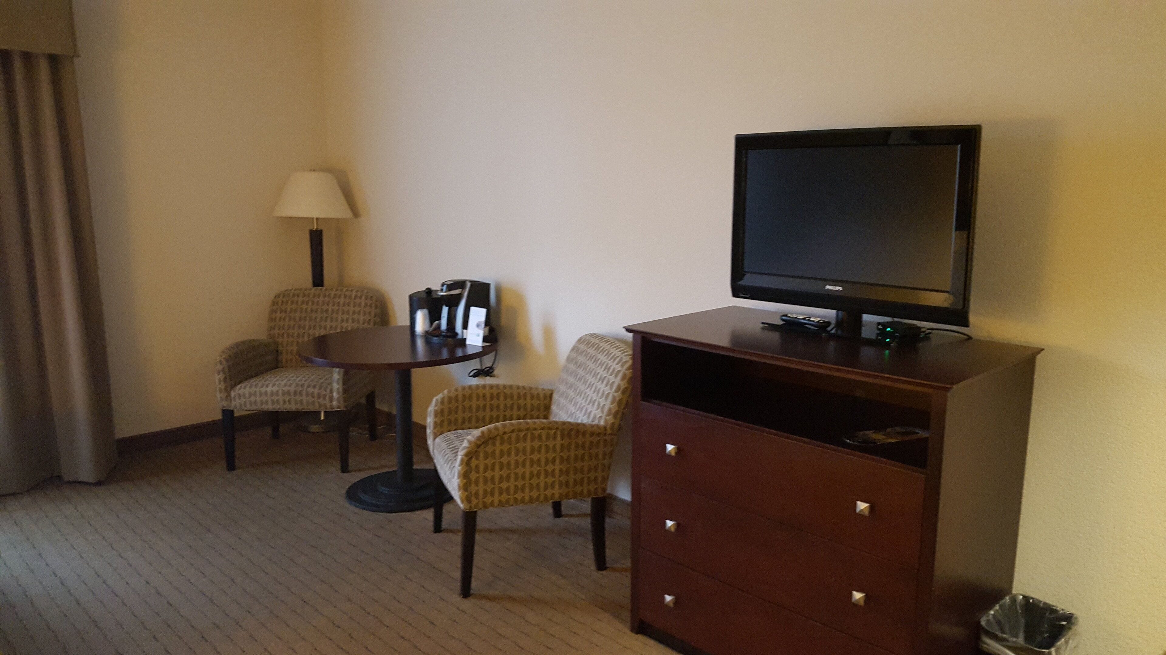A hotel room with a television, two armchairs, a small table, and a lamp.