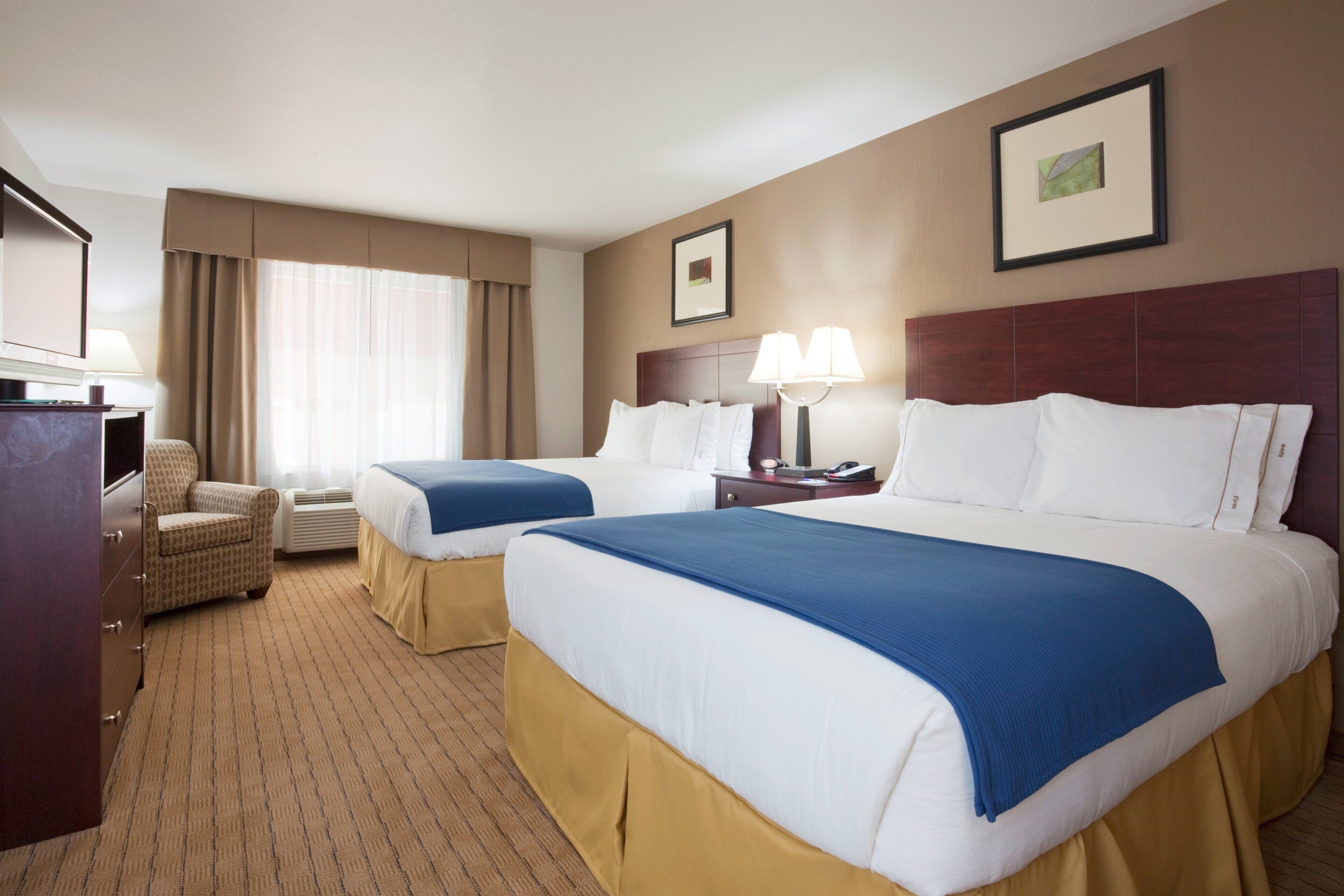 A hotel room with two beds, a desk, a chair, and a television.