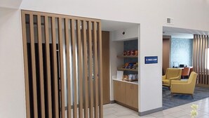 Aula, jossa on puinen sermi, kyltti, jossa lukee ”PIKAKAUPPA”, ja oleskelualue, jossa on keltaisia tuoleja.