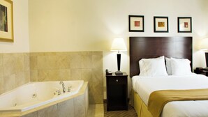 A hotel room with a large bathtub, a bed with white linens, two bedside lamps, and three framed pictures on the wall.