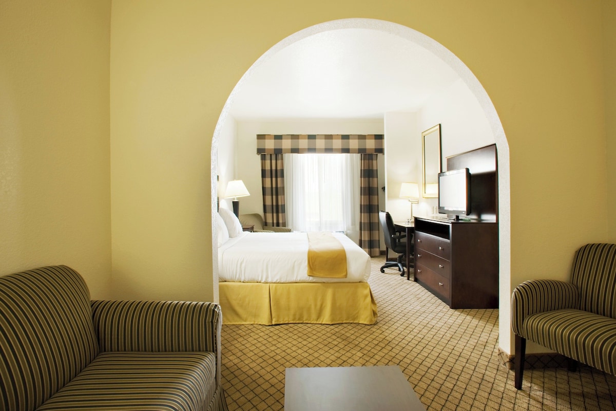 A hotel room with a bed, two armchairs, a desk, and a television.