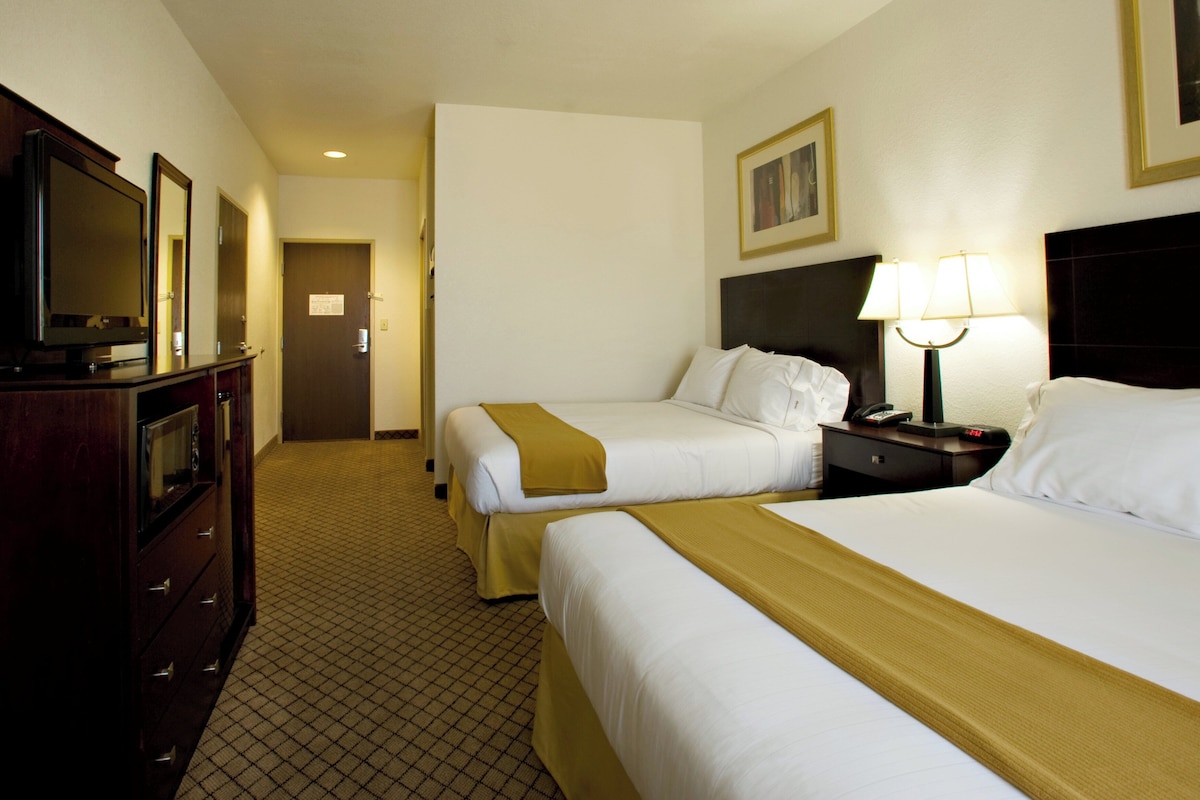 A hotel room with two beds, a TV, a desk with a lamp, and a door.