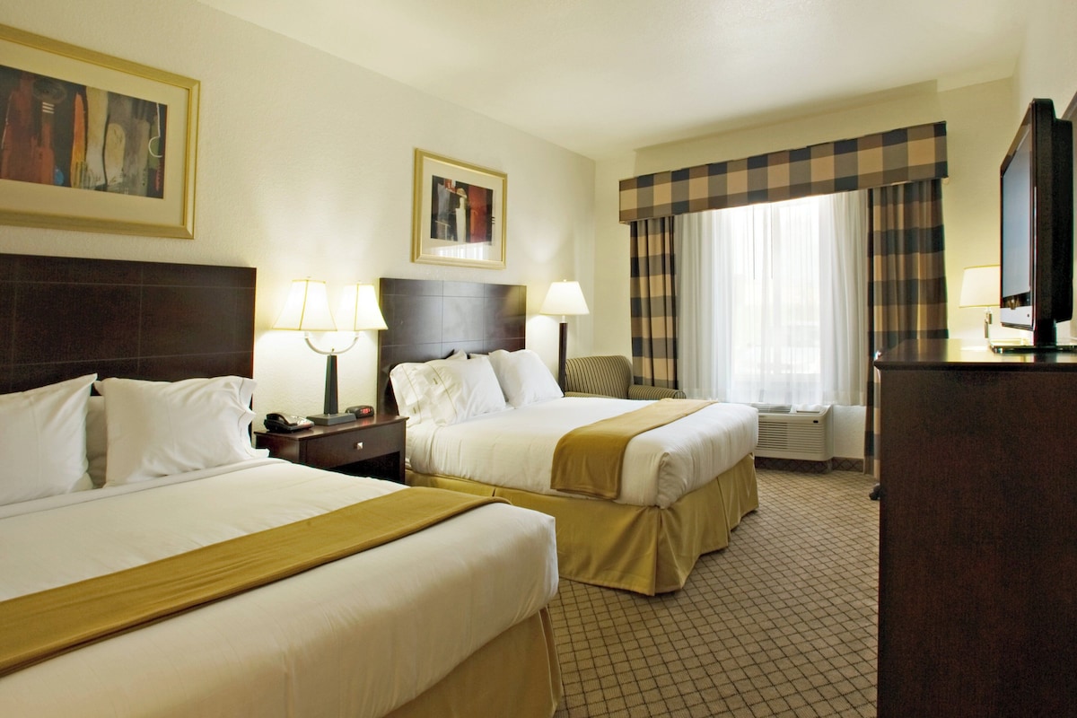 A hotel room with two beds, a desk, a television, and a window with curtains.