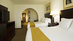 A hotel room with two beds, a TV, a desk, and a lamp.