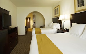 A hotel room with two beds, a TV, a desk, and a lamp.