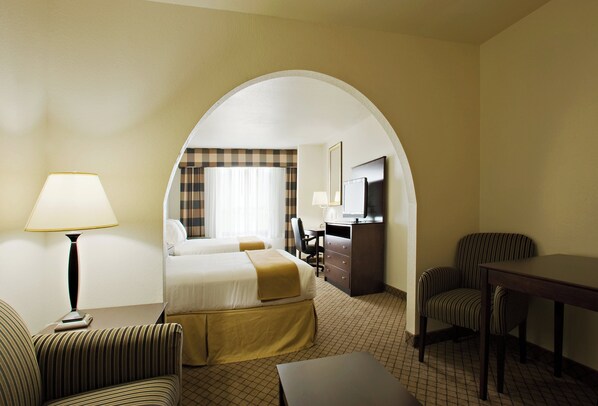 A hotel room with a bed, a desk, a chair, a lamp, and a TV.