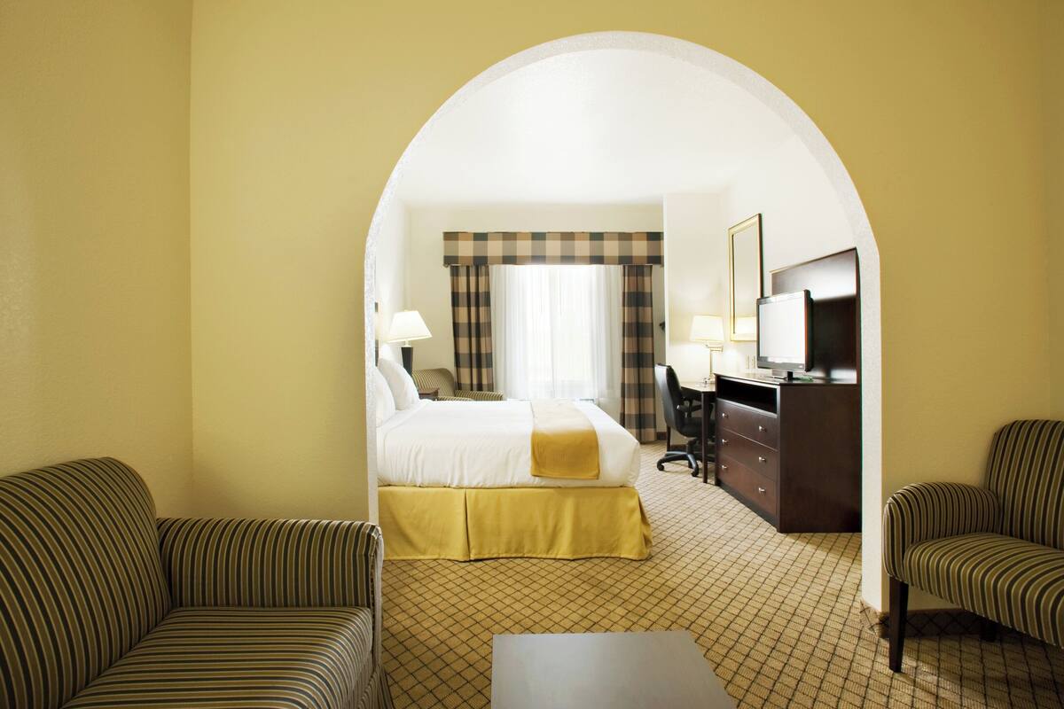 Ein Hotelzimmer mit einem Bett, zwei Sesseln, einem Schreibtisch und einem Fernseher.