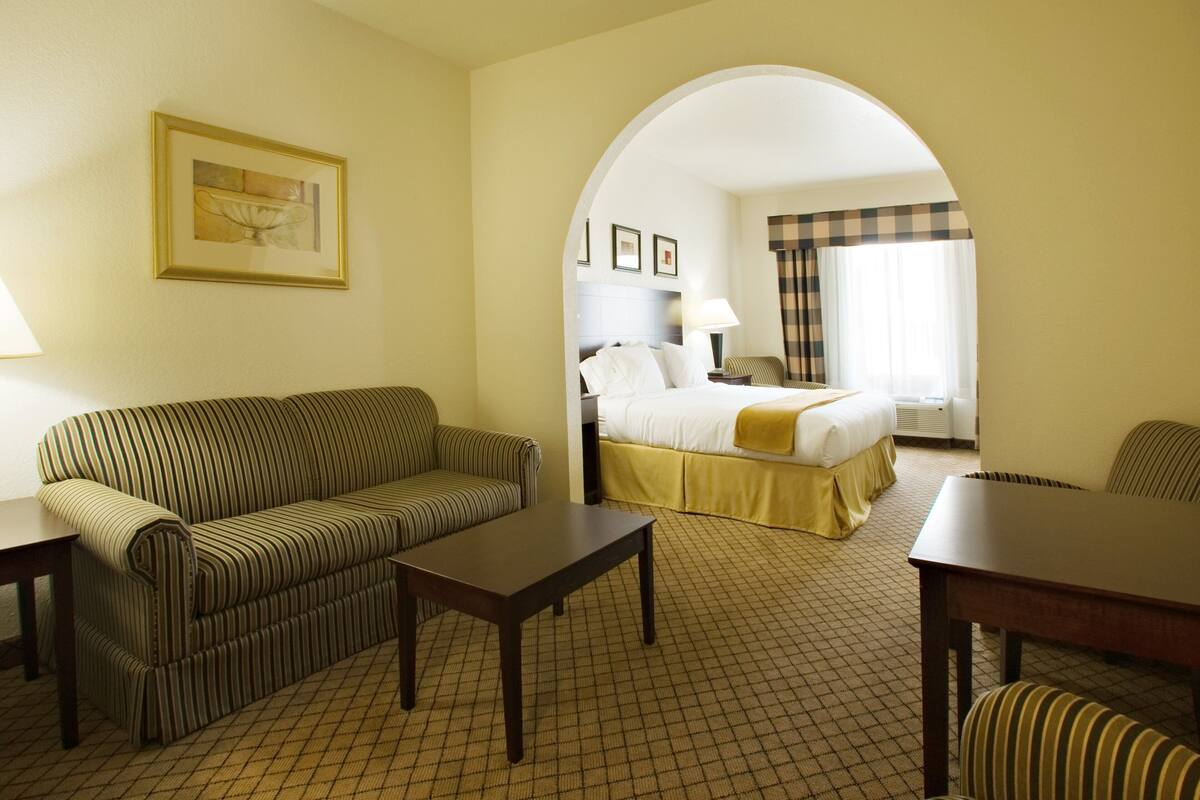 Ein Hotelzimmer mit einem gestreiften Sofa, einem Bett mit gelber Bettdecke, einem kleinen Tisch und einem Stuhl.