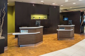 Un área de recepción con dos mostradores, una pared verde con plantas en macetas y suelo de madera.