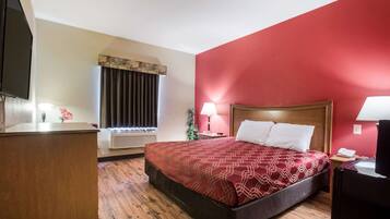 Une chambre d’hôtel avec un grand lit, un bureau, une télévision, une fenêtre avec des rideaux et un mur rouge.