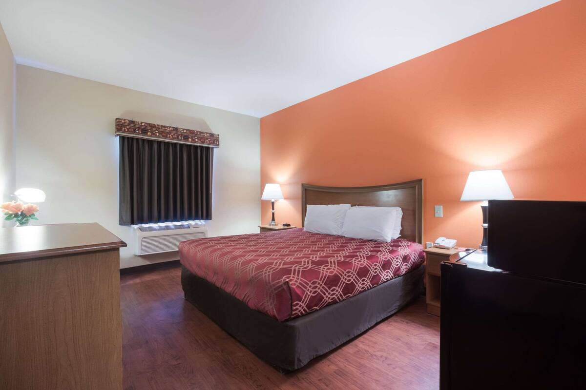 A hotel room with a bed, bedside lamps, a desk, and a television.