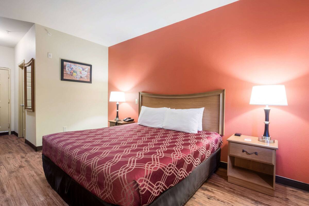 A hotel room with a large bed, two bedside tables with lamps, a wooden headboard, and a door leading to another room.