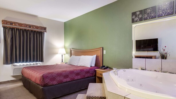 A hotel room with a bed, a large bathtub, a TV, and a green wall. - Econo Lodge Inn & Suites Rockmart (Rockmart)