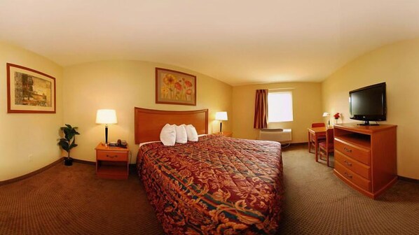 A hotel room with a large bed, a desk with a chair, a television, and two bedside lamps.