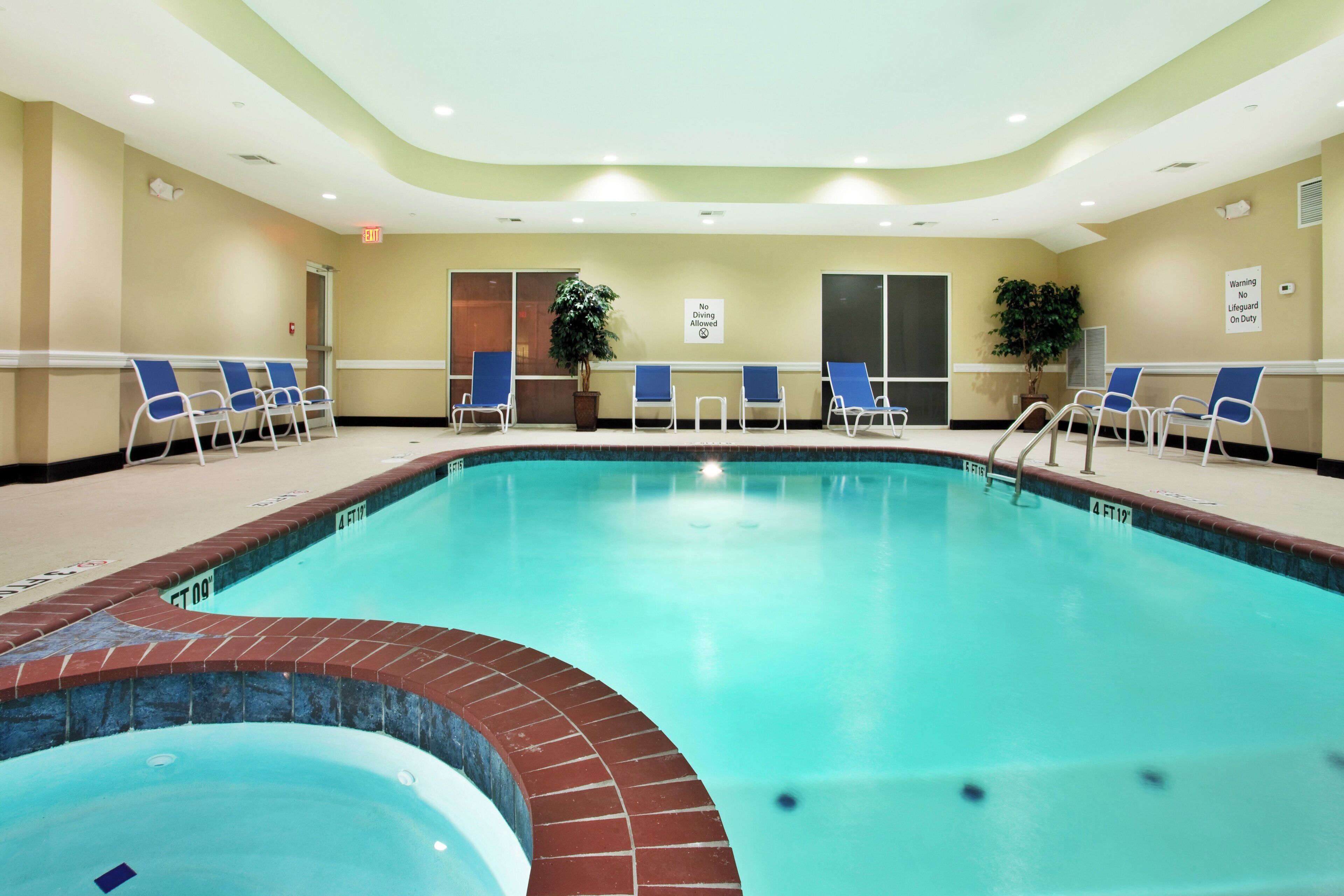 Zona de piscina de hotel con una piscina despejada, sillas azules y un letrero que indica 'No se permite el clavado'.