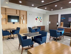 A modern cafe interior with wooden paneling, blue upholstered chairs, and a flat-screen TV mounted on the wall.