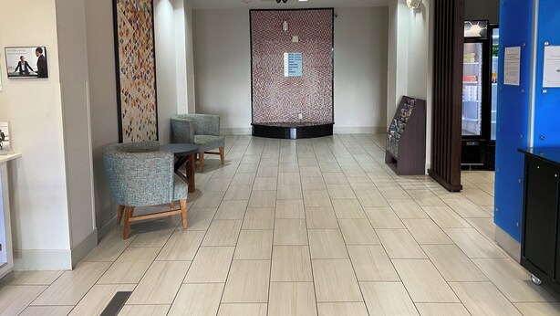 A reception area with a tiled floor, two armchairs, a wall-mounted information board, and a blue counter with a refrigerator. - Holiday Inn Express Eunice by IHG (Eunice)