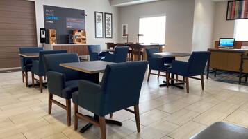 A modern dining area with blue chairs and tables, a coffee station, and a TV screen.