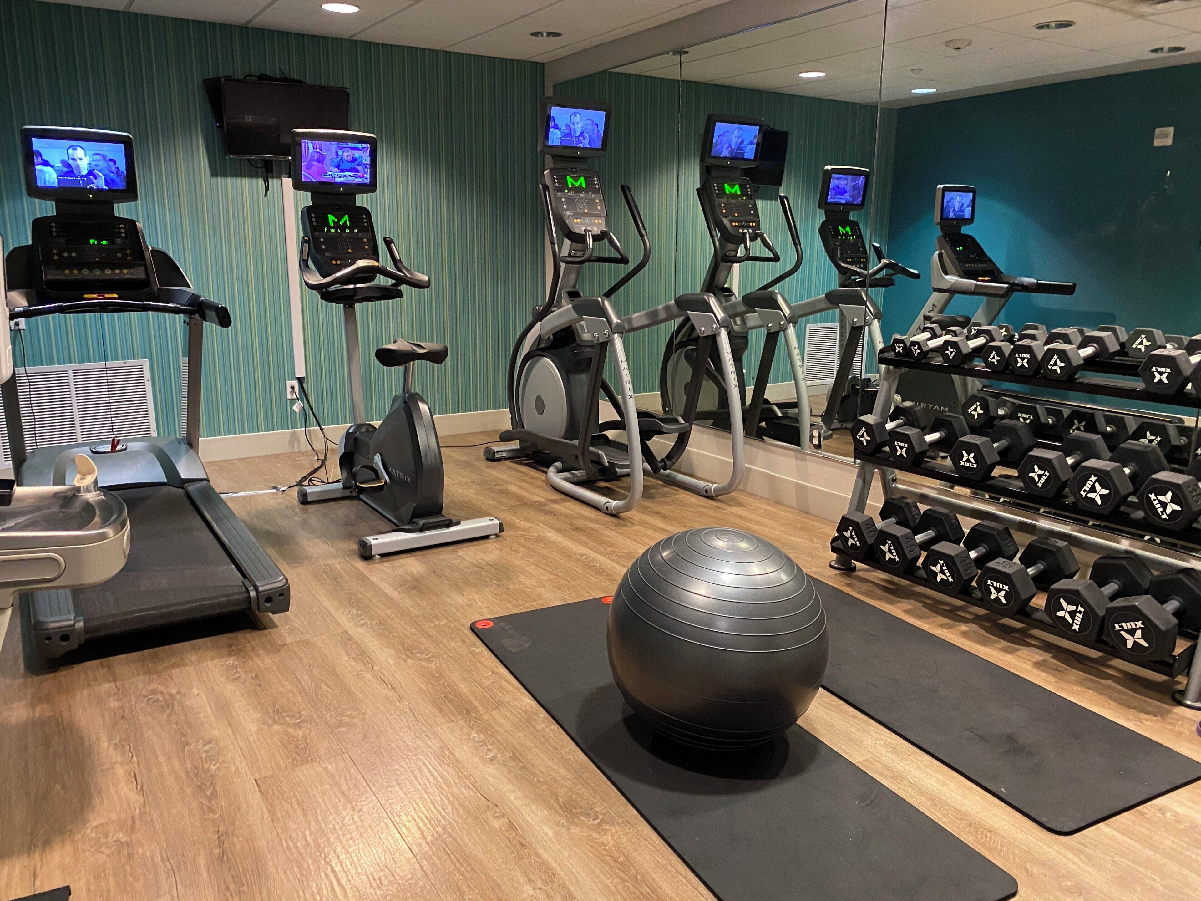 A gym with treadmills, elliptical machines, and a rack of dumbbells.