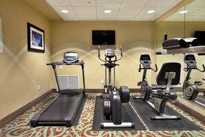 A fitness room with treadmills, elliptical machines, and a television on the wall.
