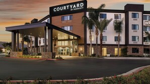 Un hotel Courtyard by Marriott con una entrada cubierta, palmeras y cielo despejado.