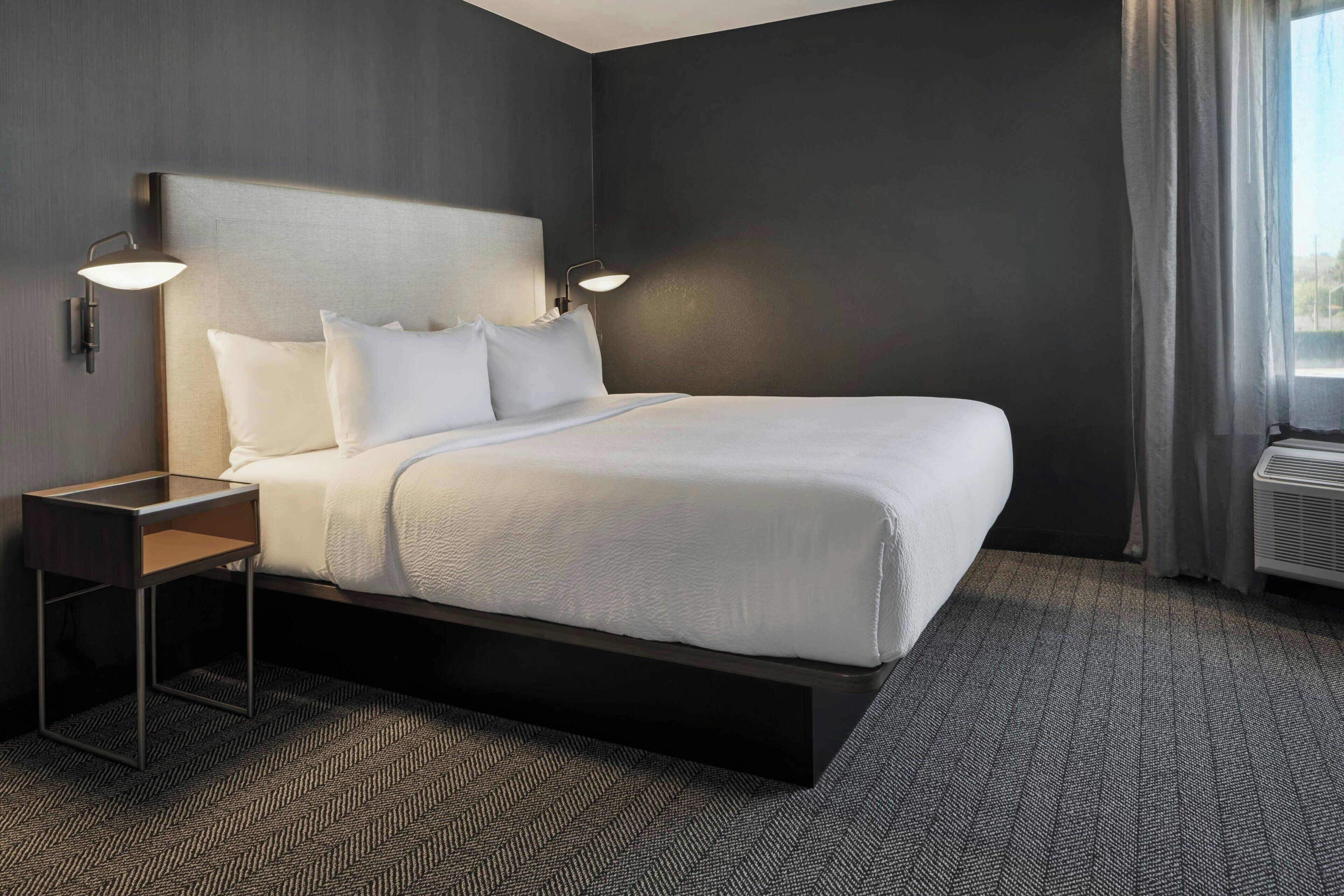 A modern hotel room with a large bed, two bedside tables, and a window with curtains.