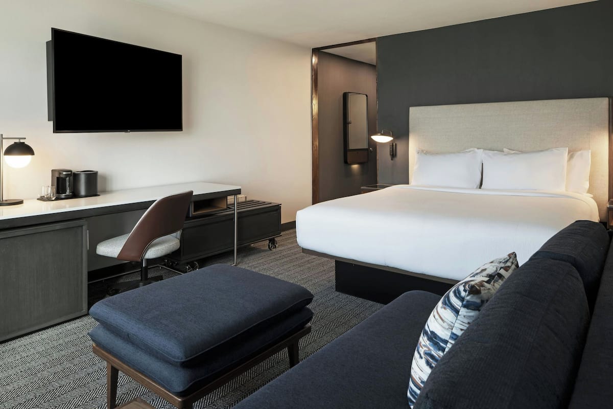 Une chambre d’hôtel équipée d’un lit, d’un bureau, d’une chaise, d’un canapé, d’une télévision et d’un miroir.