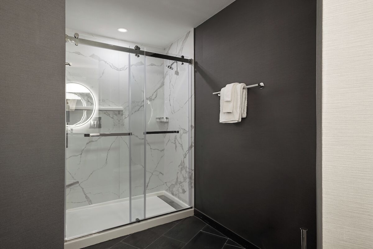 A modern bathroom with a glass-enclosed shower, a towel rack, and a marble wall.