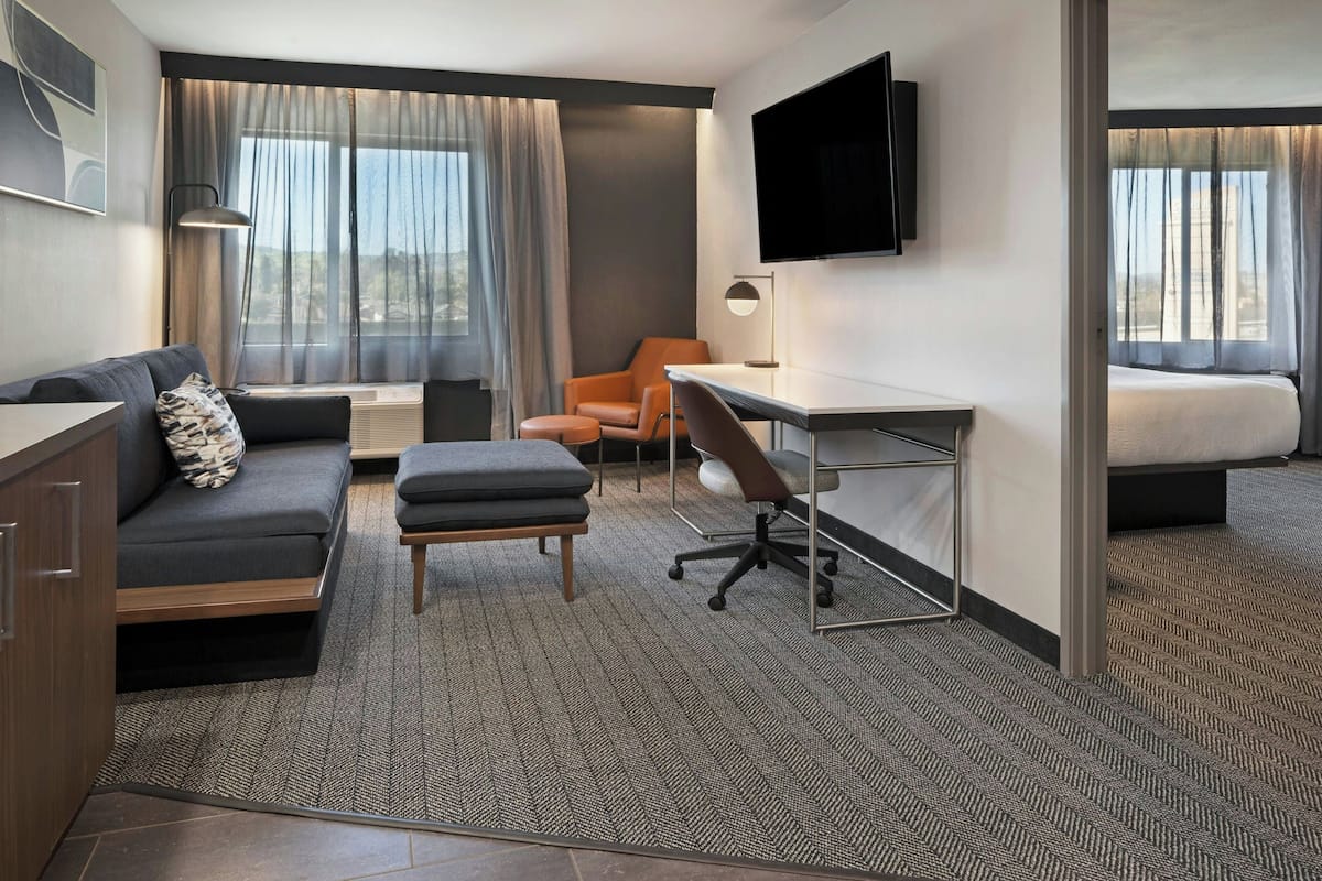 Une chambre d’hôtel équipée d’un canapé, d’un pouf, d’un bureau, d’une chaise, d’une télévision et d’un lit.