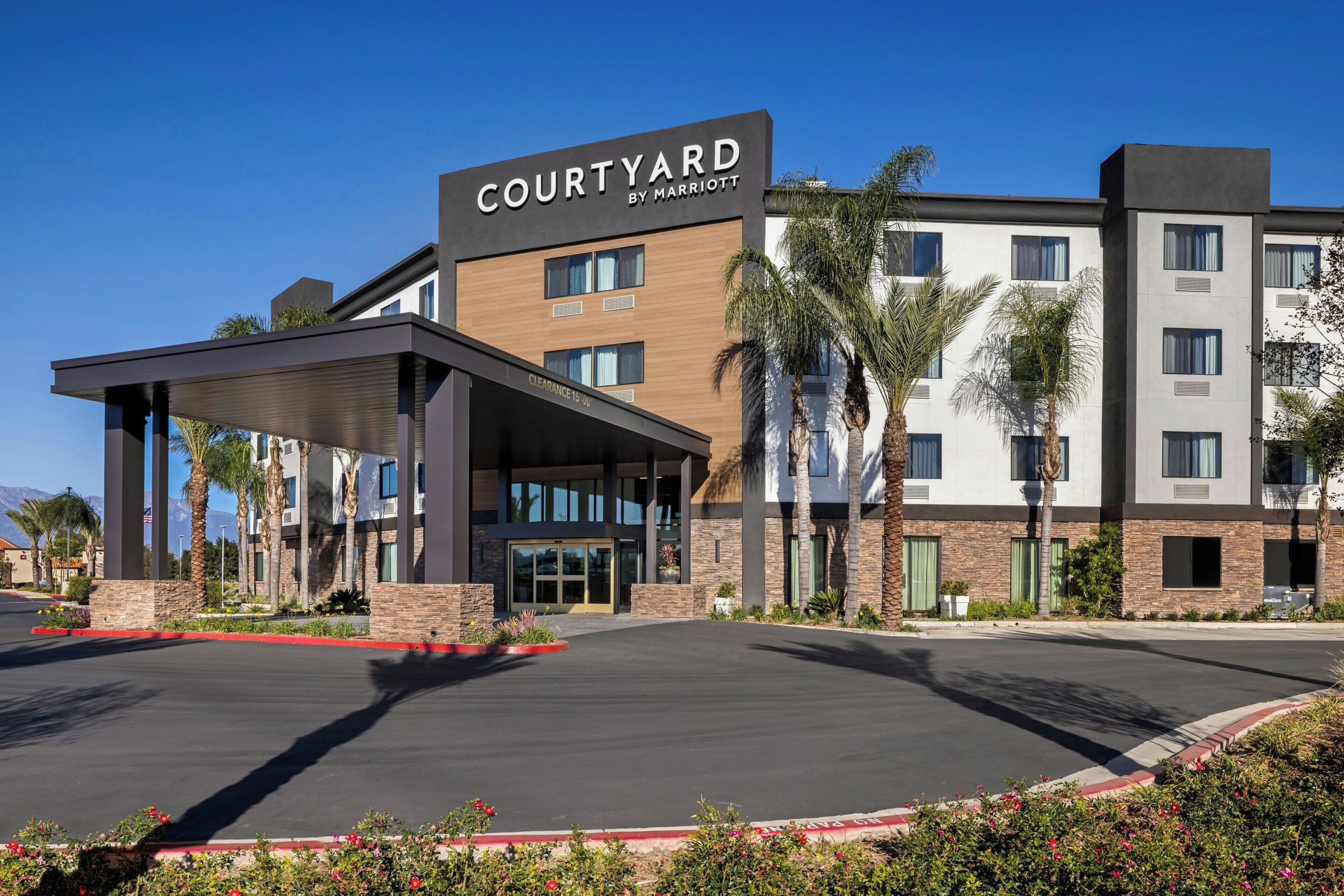 A Courtyard by Marriott hotel with a covered entrance, palm trees, and a clear sky.