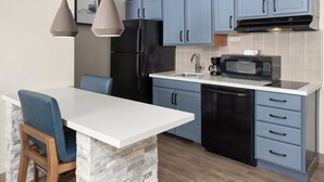 Una cocina con gabinetes azules, un refrigerador negro, un microondas y una encimera blanca.