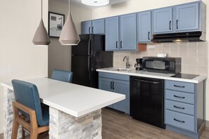 Eine Küche mit blauen Schränken, einem schwarzen Kühlschrank, einer Mikrowelle und einer weißen Arbeitsplatte.