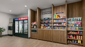 Una zona de cocina americana con refrigerador, microondas y estantes llenos de refrigerios y bebidas.