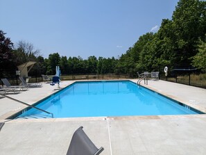Ein rechteckiger Swimmingpool mit klarem, blauem Wasser, umgeben von einer Betonplattform. Liegestühle und eine kleine, überdachte Sitzgelegenheit sind vorhanden.