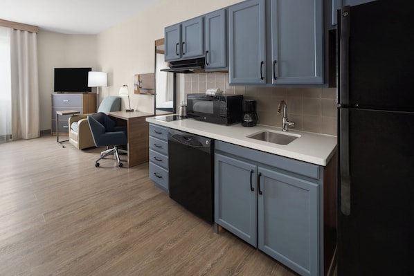 A modern kitchen with grey cabinets, a black refrigerator, a microwave, and a coffee maker.