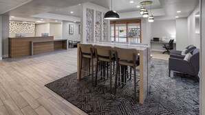 A modern office space with a reception desk, a bar area with stools, a sofa, and a patterned rug.