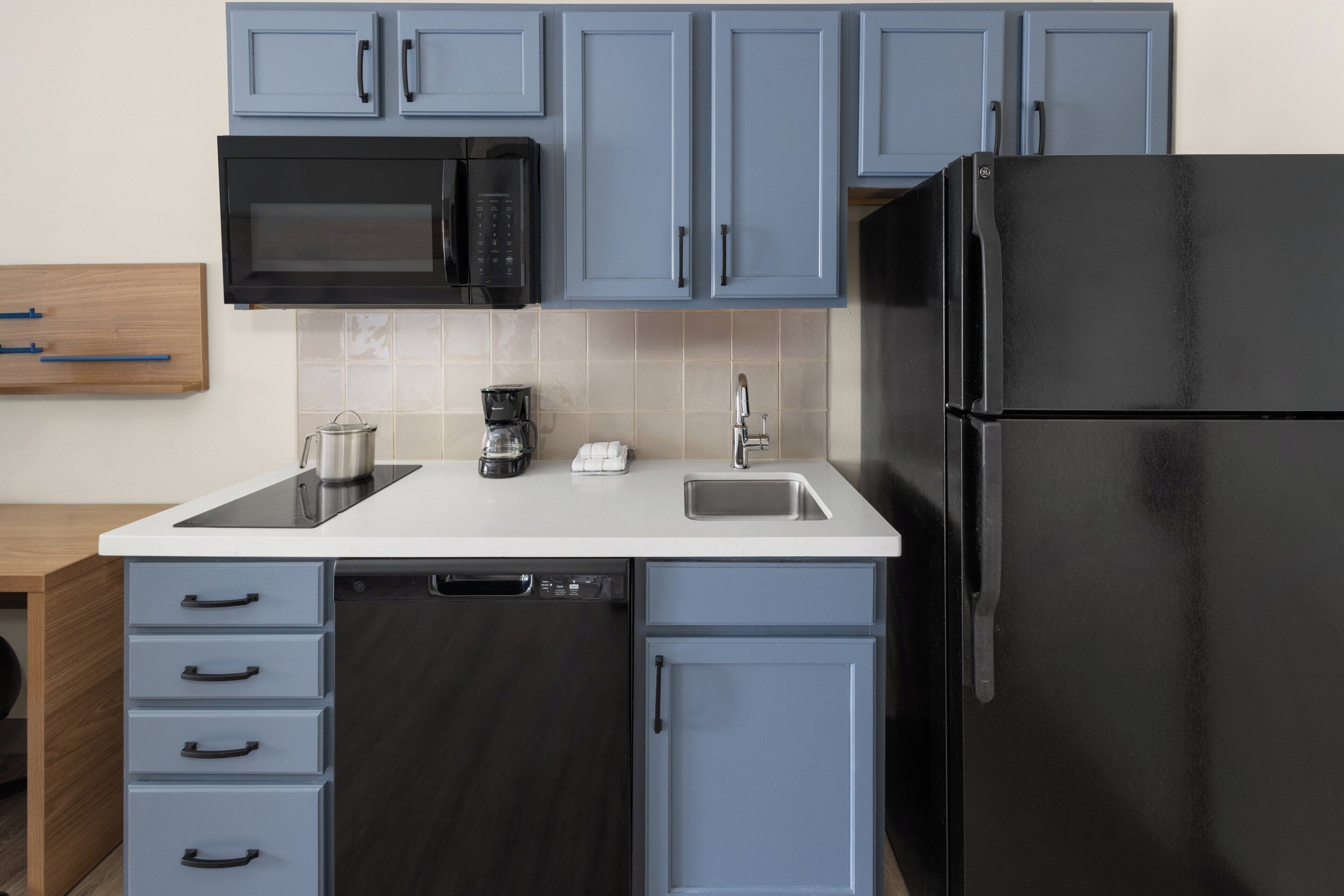 A modern kitchen with blue cabinets, a black refrigerator, a microwave, and a dishwasher.