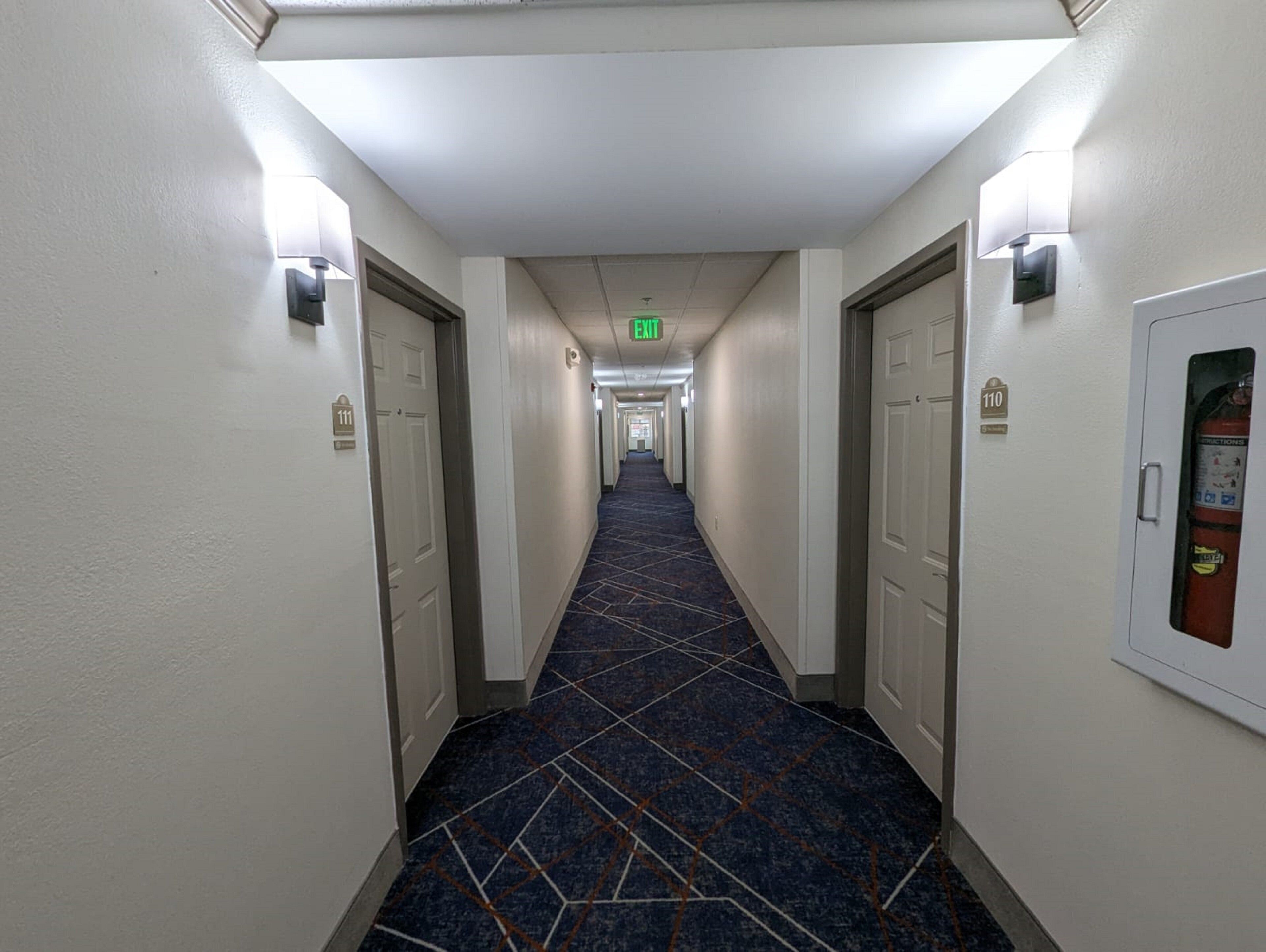 A hotel hallway with a blue patterned carpet, white walls, and doors numbered 111 and 110.