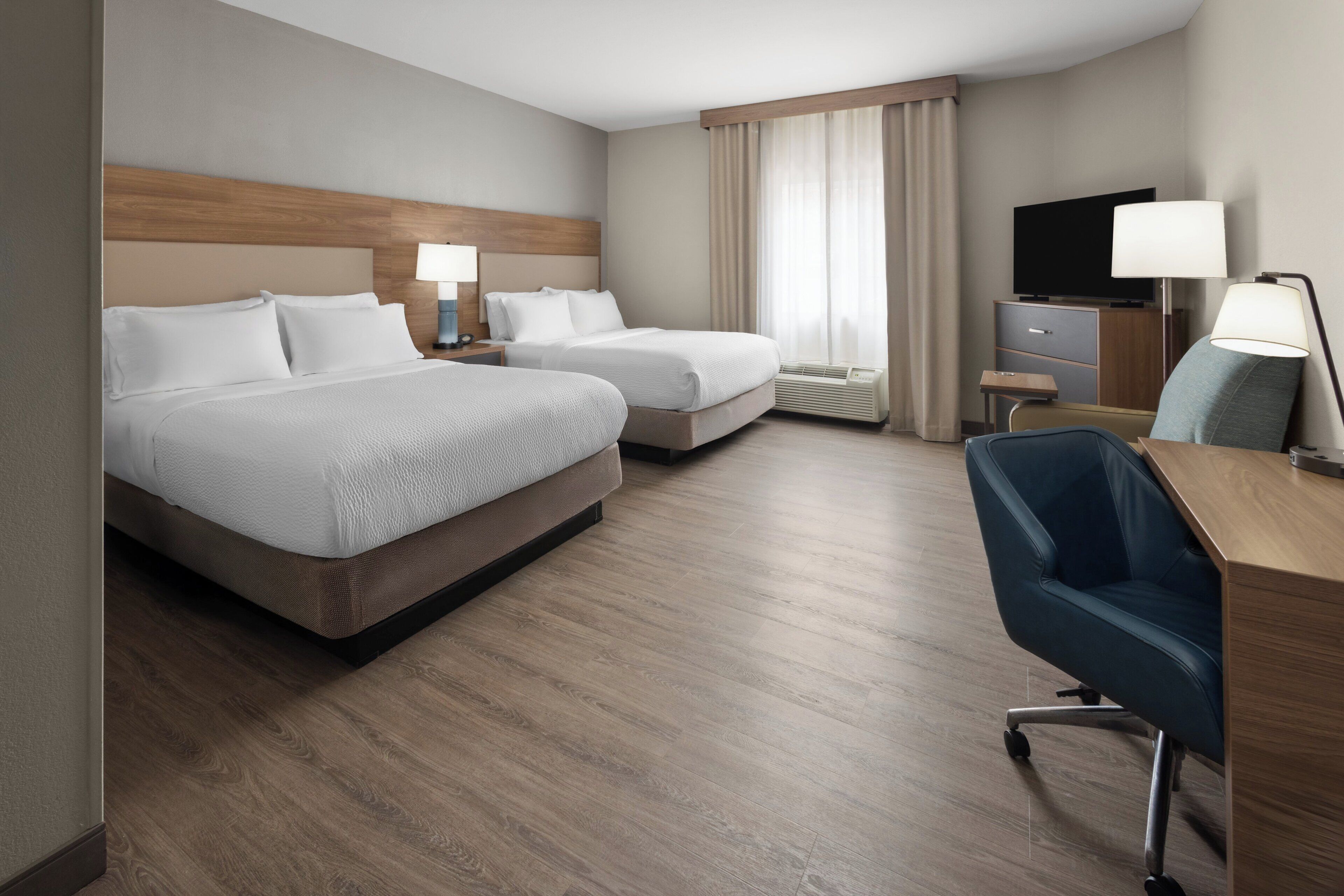 A hotel room with two beds, a desk, a chair, a TV, and a window with curtains.