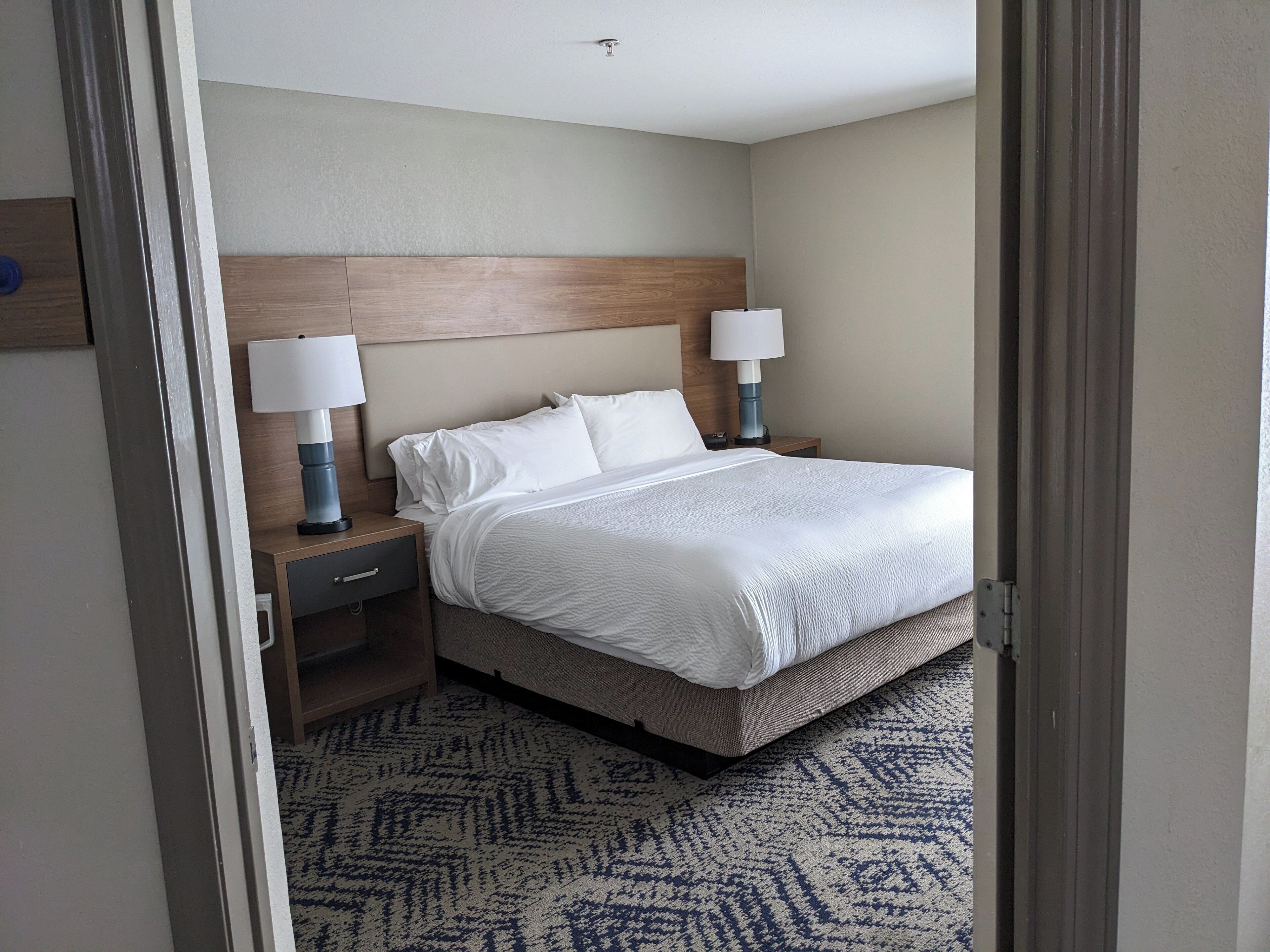 Una habitación de hotel con una cama, dos lámparas de noche, una mesita de noche y una alfombra estampada.